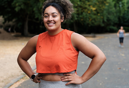 Portrait of smiling young woman standing on a road park and looking at camera. Curly hair. Sleeveless orange t-shirt.