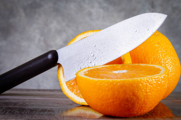 istock Slicing oranges side view. A man cuts an orange with a knife.  Knife and orange. 1417737094