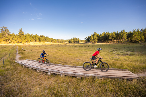 Two Boys Riding Their Mountain Bikes across a wooden bridge in a meadow at sunset in Mt Laguna, Cleveland National Forest, California.  Big Laguna Trail.