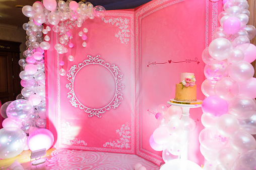Pink photo zone with book, balloons, pearls and cake on birthday party