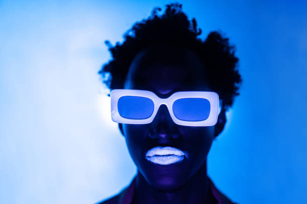 An unrecognizable person backlit by blue light, with illuminated neon sunglasses and lips
