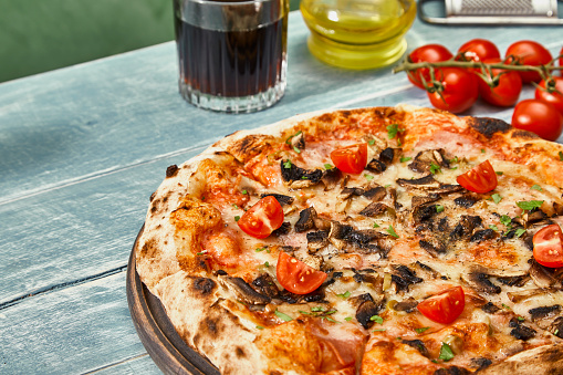 Colorful Pizza on a rustic kitchen or restaurant table, with fresh cherry tomato, olive oil and coke, with a copy space