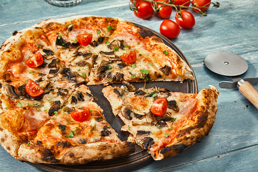 Pizza with one slice separated on a rustic kitchen or restaurant table, with fresh vegetables