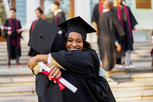 Happy young student is embracing a friend during the graduating ceremony outside the University