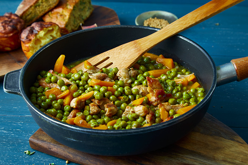Homemade peas with carrot and chicken or beef meat in a black pan, on a blue wooden table top