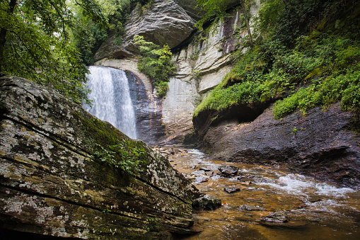 A beautiful waterfall landscape of Looking Glass Falls in North Carolina during summer with a large boulder in the foreground.