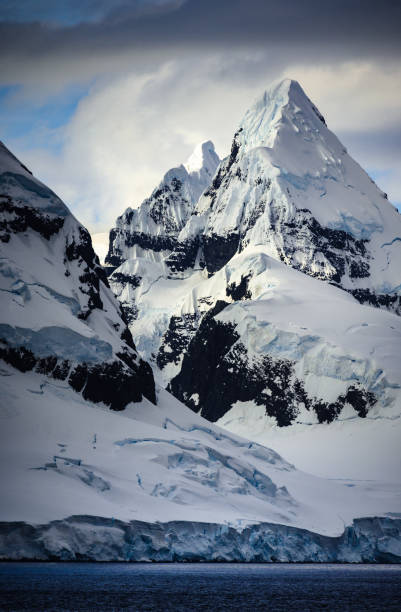 Towering mountains and snow white glaciers in a vertical composition. Glacier surface shows the crevices that develop as they slide slowly down the mountain. Eventually they break off into the sea as icebergs.