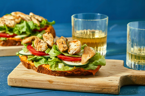 Healthy and colorful chicken sandwich with vegetables and salad on a blue wooden home or restaurant table, hipster dish