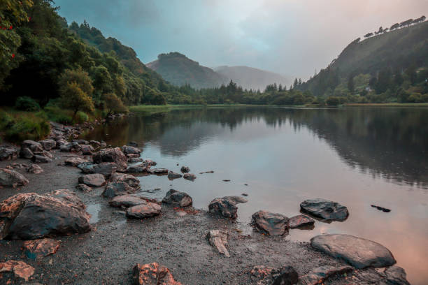 Reflections on a Celtic lake with forest and mountains with a bit of a drizzle on a hazy summer day in Glendalough, Ireland