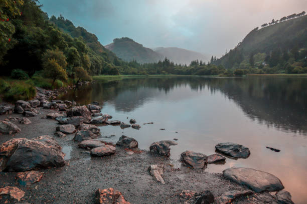 Reflections on a Celtic lake with forest and mountains with a bit of a drizzle on a hazy summer day in Glendalough, Ireland Reflections on a Celtic lake with forest and mountains with a bit of a drizzle on a hazy summer day in Glendalough, Ireland killarney lake stock pictures, royalty-free photos & images