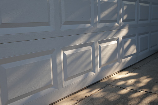 Shadows fall on a white garage door and driveway in a residential district in Surrey, British Columbia. Summer morning.