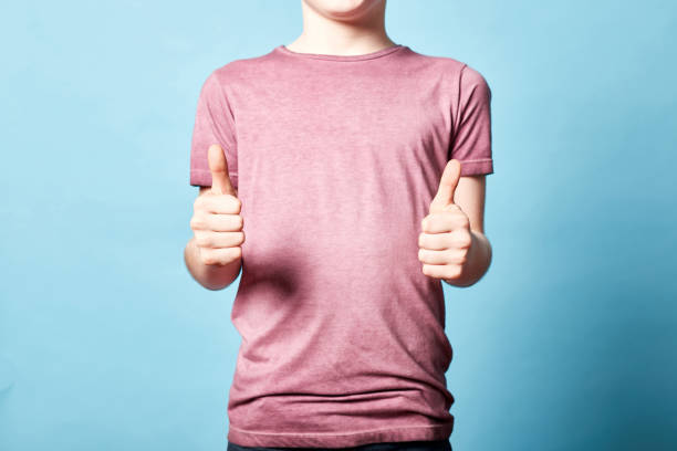 vista frontal de un niño caucásico de 10 años que muestra pulgares hacia arriba, gesto positivo con la mano aislada sobre fondo azul. espacio de copia. - 10 11 years little boys child happiness fotografías e imágenes de stock