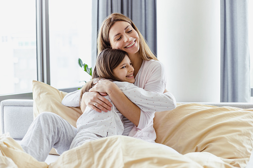 Portrait of mother and daughter embracing in bedroom