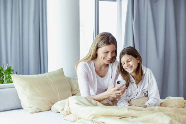 istock Beautiful young mother and her cute daughter using mobile phone in bed 1417773705