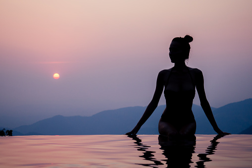Young woman relaxing in infinity swimming pool looking at view romantic sunset overlooking the hills wildernest nature spa resort in India Goa Kerala.