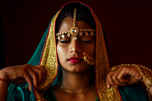portrait indian beautiful female in golden rich jewelery and tradition saree face closeup professional make-up wearing bindi on head .Muslim Woman face portrait with bindis maang tikka ,nath,nose Pin