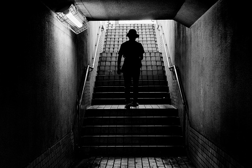 Back view of a man wearing a hat going up the stairs from the underpass