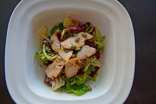 Portion of tasty salad with slices of grilled chicken breast.