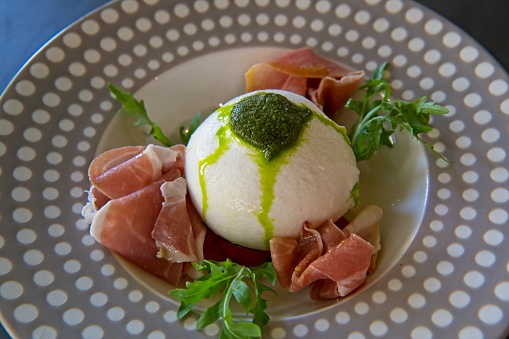 Bowl of freshly made burrata cheese served with Italian style ham and pesto.