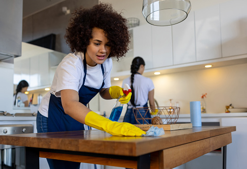 Professional Latin American cleaner cleaning a table at a house and smiling - housework concepts