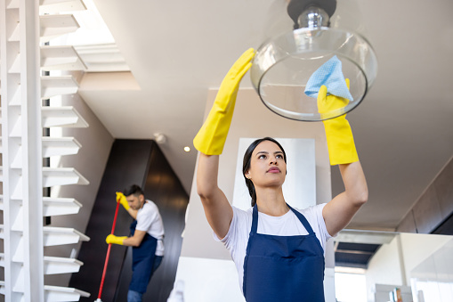 Professional Latin American housekeeper cleaning a glass lamp in the kitchen of a house - housekeeping concepts