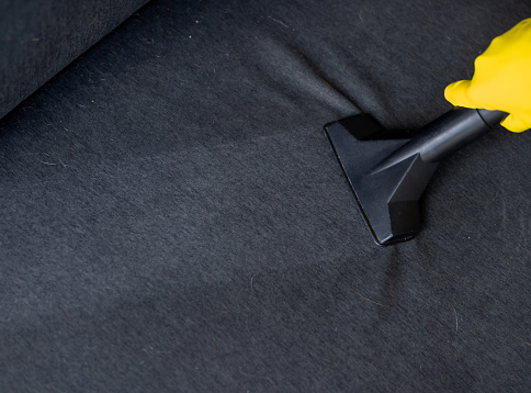 Close-up on a professional cleaner vacuuming a sofa - housework concepts