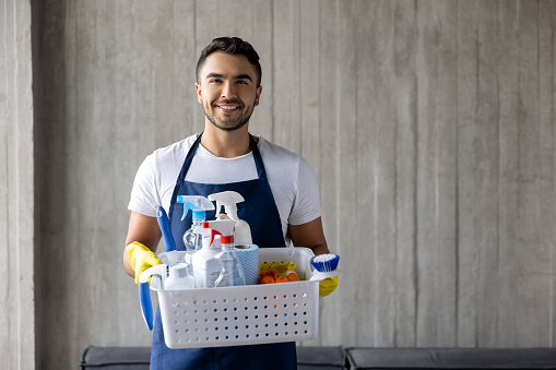 Portrait of a happy professional cleaner holding a basket of cleaning products and smiling at the camera - housework concepts