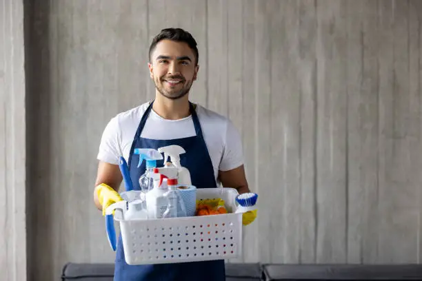 Portrait of a happy professional cleaner holding a basket of cleaning products and smiling at the camera - housework concepts