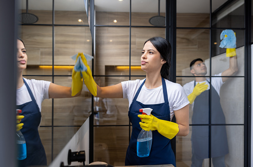 Team of professional cleaners cleaning the mirror and glass in the bathroom - housekeeping concepts