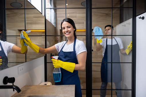 Happy professional cleaners cleaning a bathroom at an apartment and looking at the camera smiling - housework concepts