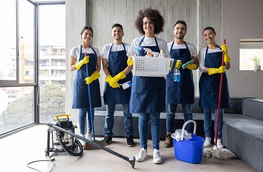 Latin American team of professional cleaners working together at an apartment and looking at the camera smiling