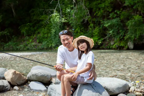 Photo of Young father and his little daughter fishing on a riverbank.