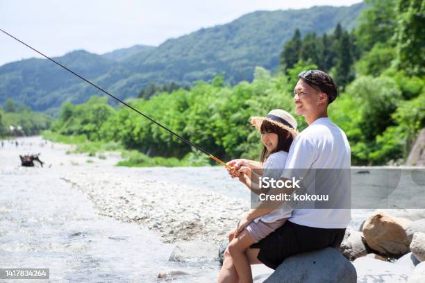 若い父親と幼い娘が川岸で釣りをしています。