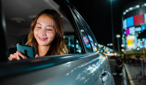 азиатская бизнесвумен добирается из офиса на заднем сиденье такси с мобильным телефоном в дороге - luxury car women smart phone стоковые фото и изображения