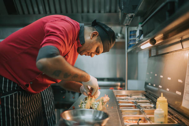 One man, male workers making burrito in fast food restaurant, he is standing behind the counter.