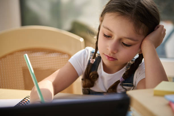 istock Close-up of a 5 years old Caucasian schoolgirl making notes while watching broadcasted online lesson on a digital tablet 1417843862