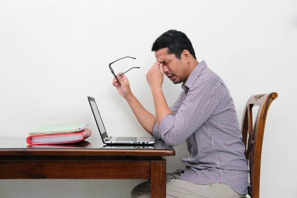 side view of asian man sitting in front of laptop showing tiredness - pusing imagens e fotografias de stock