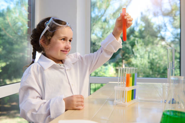 caucasian preschooler girl testing chemical lab experiment and holding flask with orange liquid during chemistry lesson - reagent imagens e fotografias de stock