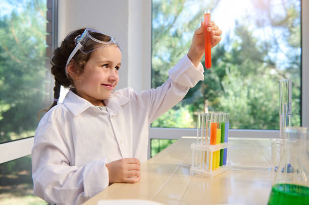 кавказская дошкольница тестирует химический лабораторный эксперимент и держит колбу с оранжевой жидкостью во время урока химии - reagent стоковые фото и изображения