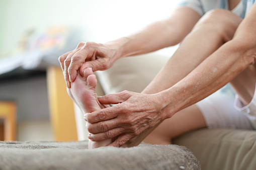 Closeup Senior woman sitting on sofa massaging her feet feeling pain. Health care and medical concept.