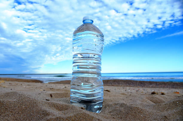 Plastic bottle with mineral water on beach by sea. PET bottle on the sand. Plastic trash thrown into the ocean. Thirst for water during dry and hot weather. Clean water in bottle at coastline.