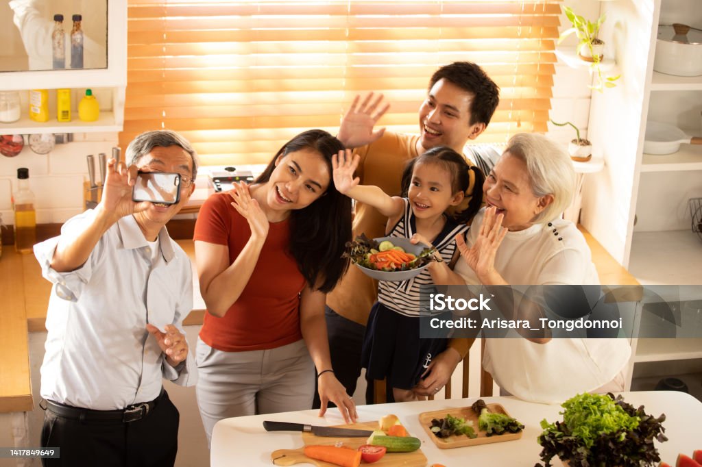 A large family is taking selfies in the kitchen. Happy big Asian family preparing for cooking healthy food and taking selfies with smart phone in kitchen 25-29 Years Stock Photo