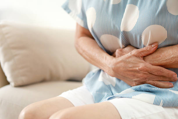 Senior woman having painful stomachache, sitting on sofa at home stock photo