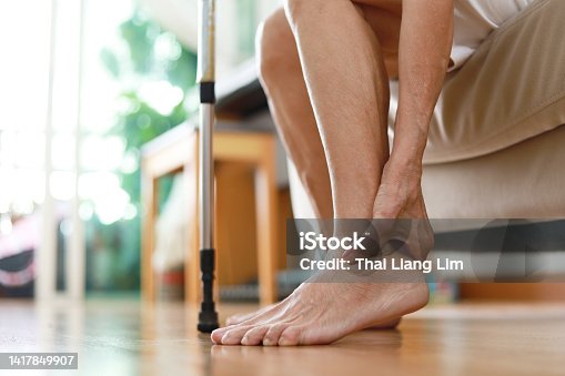 istock Senior woman sitting on sofa holds her ankle injury, feeling pain. 1417849907