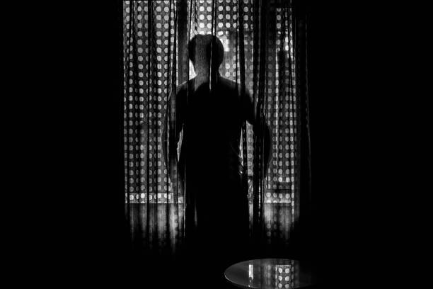 Silhouette through the curtains of a man looking out the window