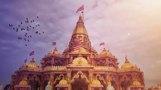 Beautiful hindu god temple with birds in the sky at sunrise time with flags and cloudy sky.