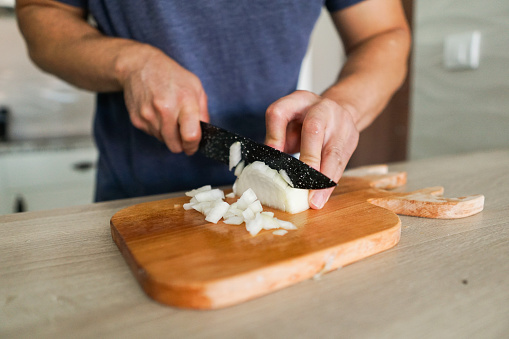 A man chopping onions with a kitchen knife on wooden cutting board
