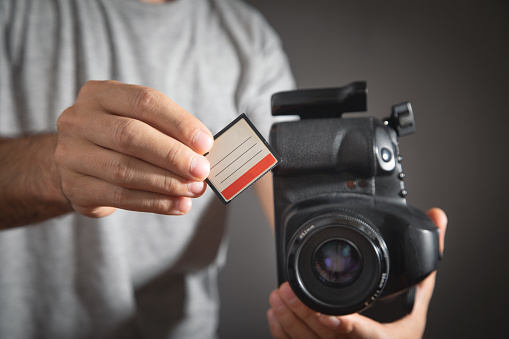 Photographer holding memory card insert DSLR camera.
