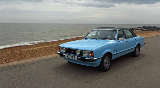 Felistowe, Suffolk, England - May 01' 2022: Classic Light Blue Ford Cortina Mk4 on seafront promenade beach and sea in background.