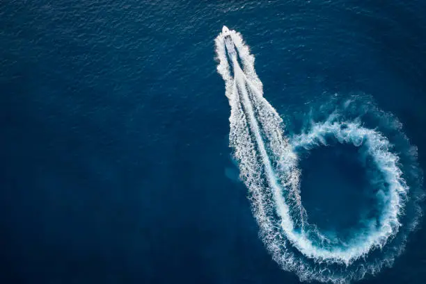 Aerial top view of a motor powerboat forming a circle of waves and bubbles with its engines over the blue sea